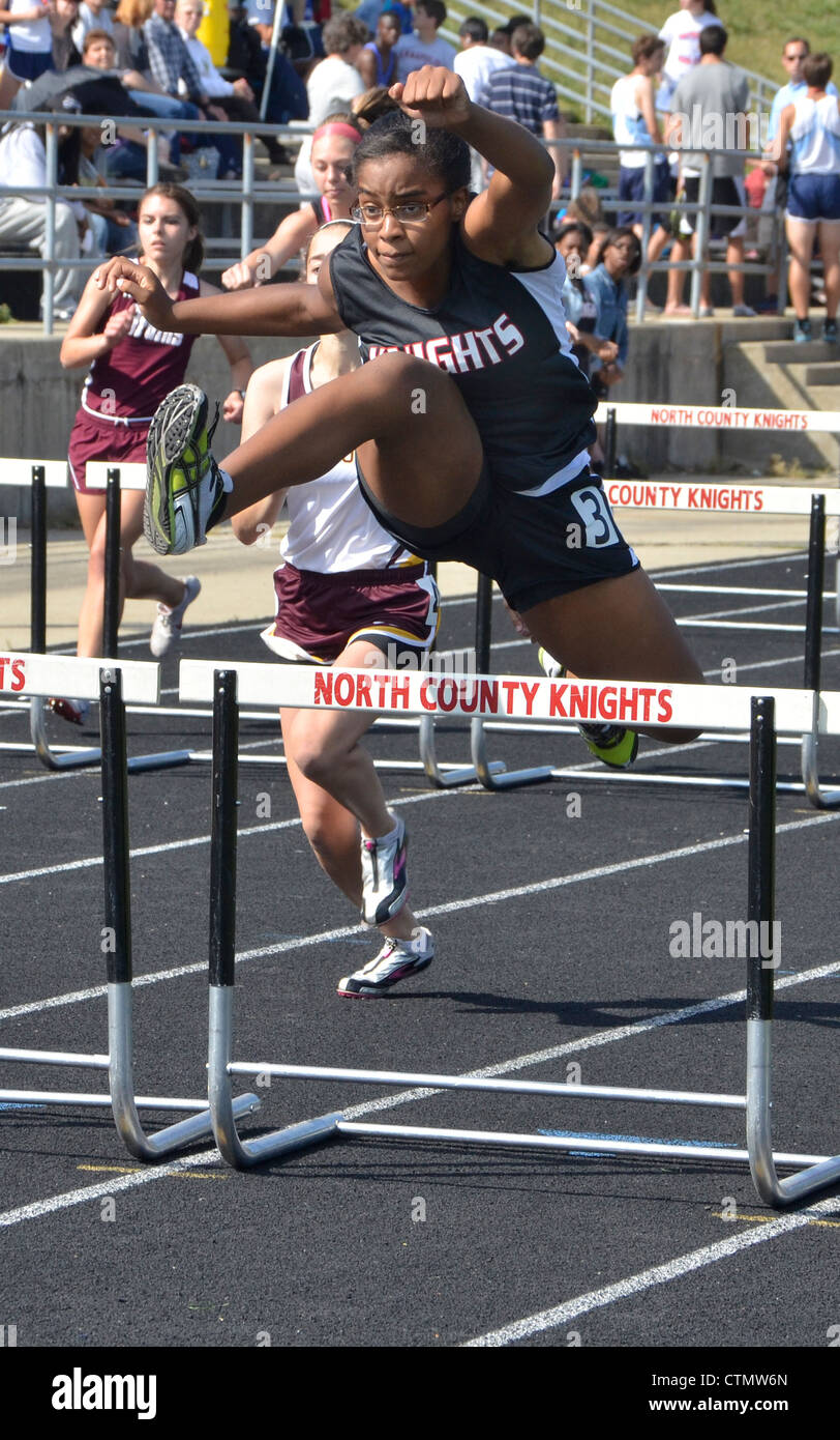 teen girl running in the hurdles in a high school track and field event