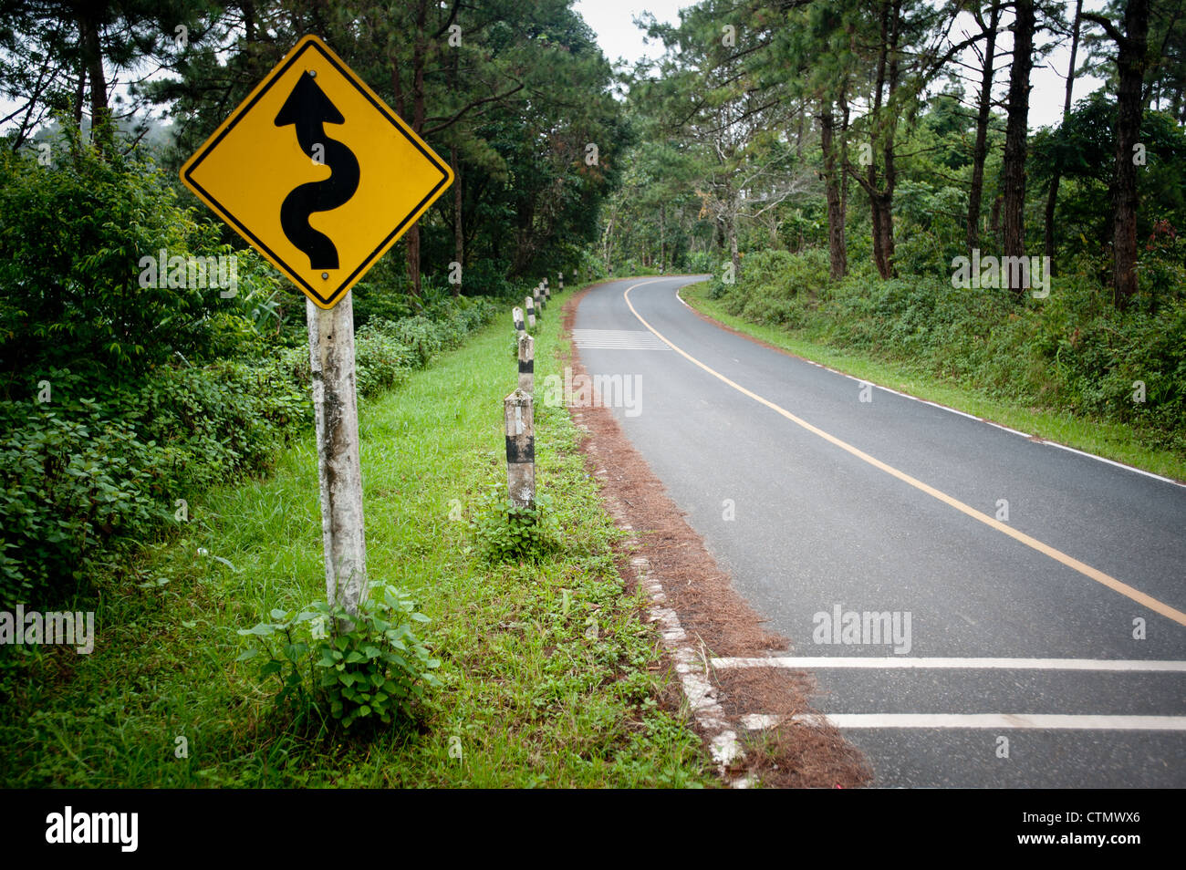 Empty road through forest with road sign warning of sharp bends ahead in Pai, Northern Thailand, Thailand. Stock Photo