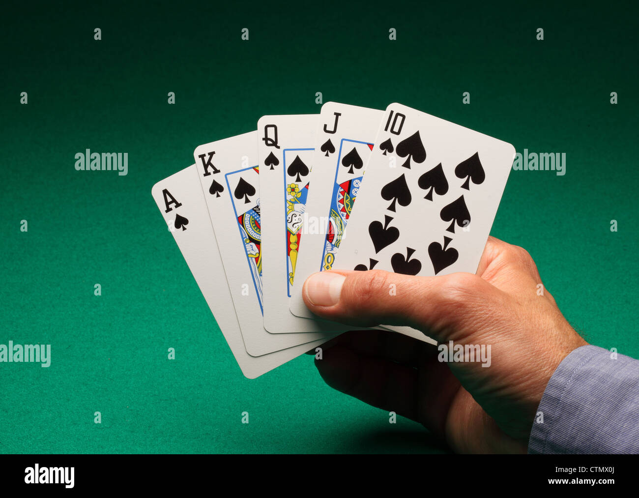 A man's hand holding playing cards on a green table. A Royal Flush of spades in the game of Poker Stock Photo