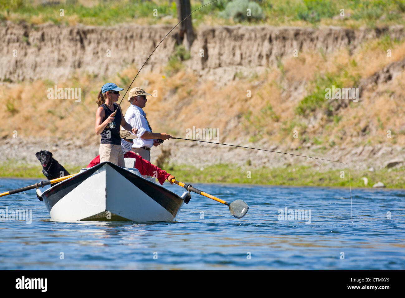 A guide maneuvers his drift boat while a woman and man fly fish the