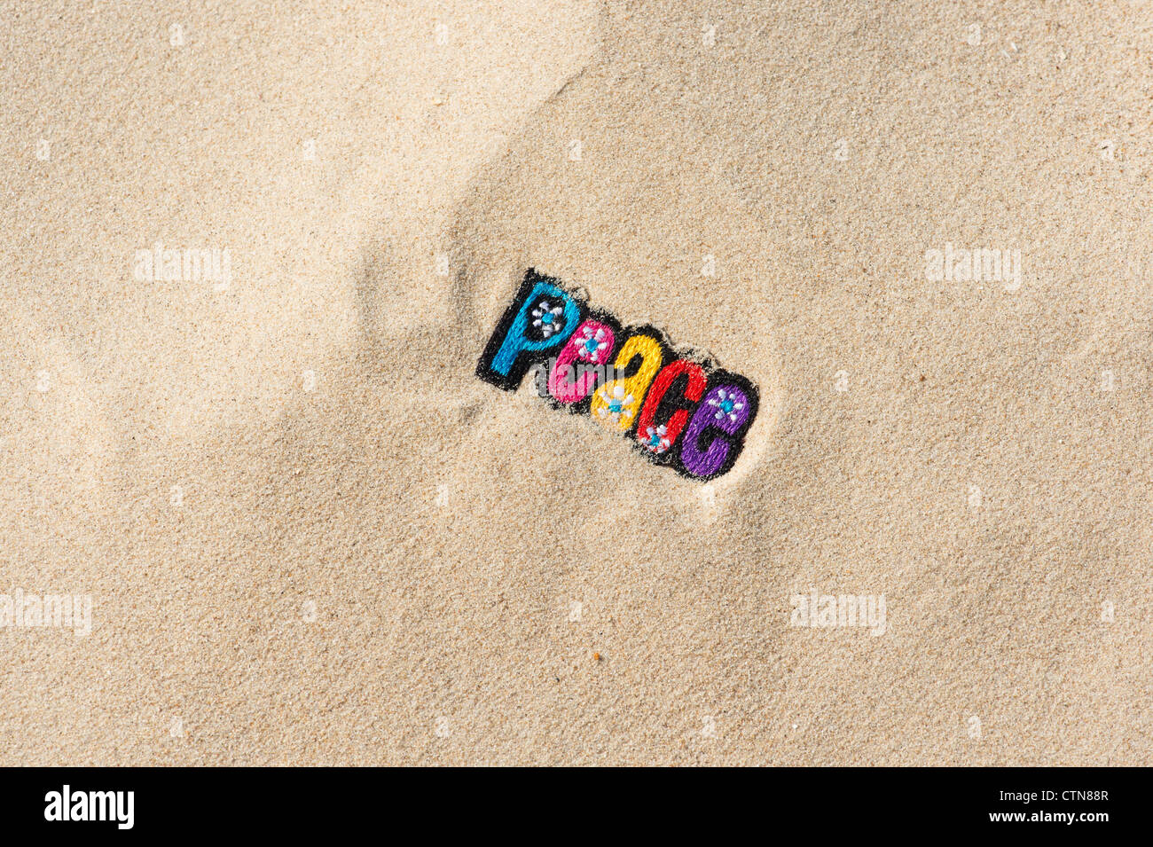 Multicoloured embroidery iron on PEACE patch in sand on a beach Stock Photo