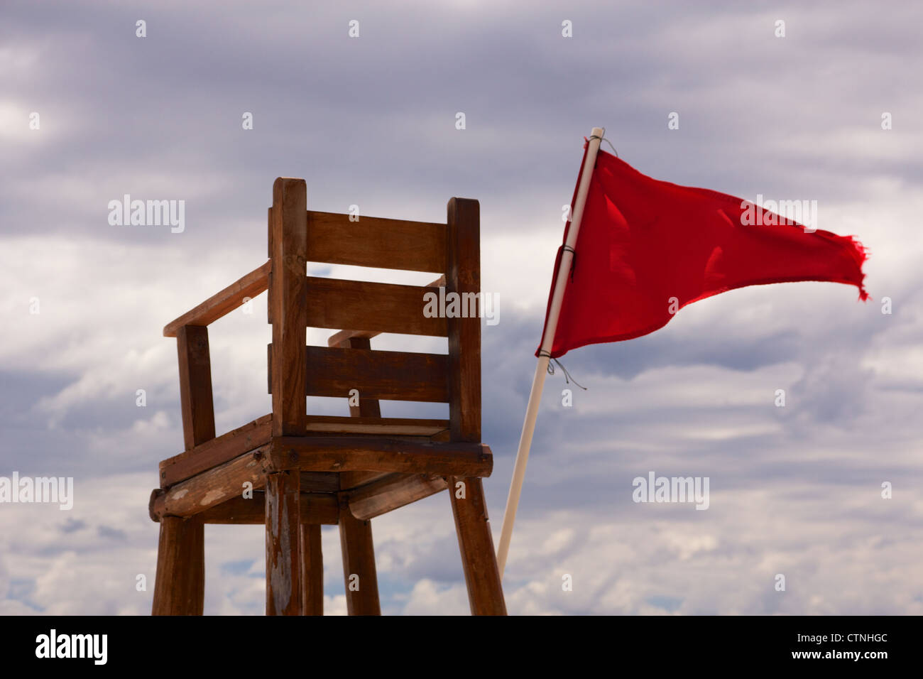 Lifeguard chair sitting empty with a red flag streaming in the wind, showing unsafe conditions for swimming. Stock Photo