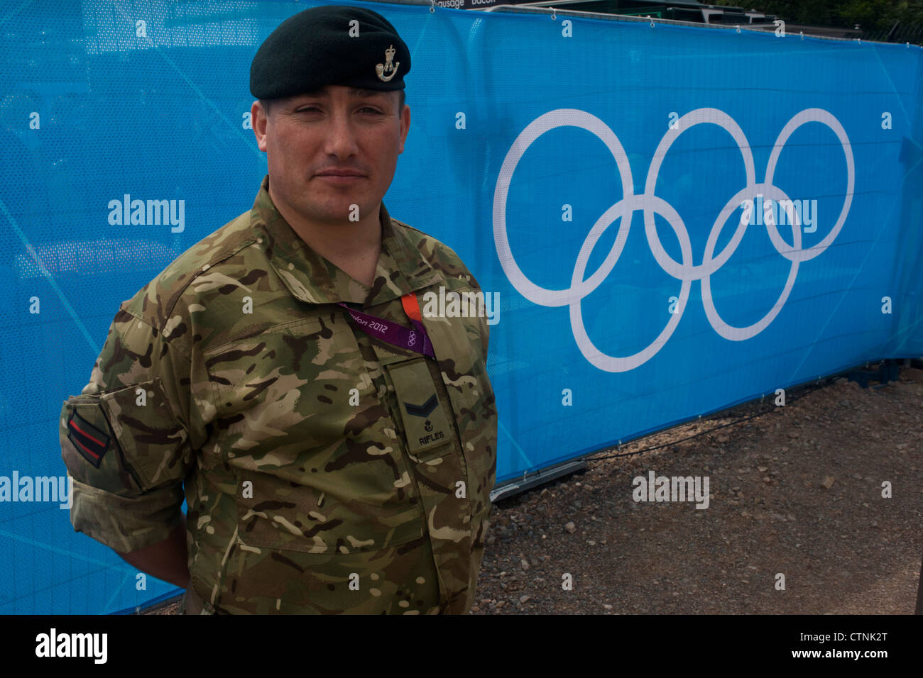 A portrait of a Lance Corporal in the Rifles regiment of the British army next to the Olympic rings logo before the start of the canoe slalom heats at the Lee Valley White Water Centre, north east London, on day 3 of the London 2012 Olympic Games. A further 1,200 military personnel are being deployed to help secure the 2012 Olympics in London following the failure by security contractor G4S to provide enough private guards. The extra personnel have been drafted in amid continuing fears that the private security contractor's handling of the £284m contract remains a risk to the Games. Stock Photo