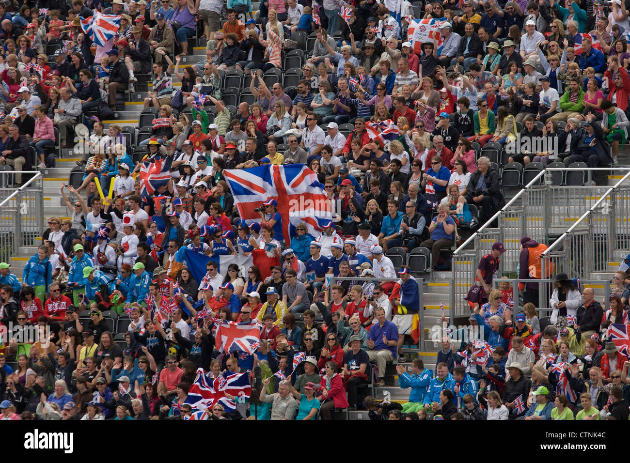 British fans hold up Union Jack flags surrounded by crowds of sports supporters seem en mass during the canoe slalom heats at the Lee Valley White Water Centre, north east London, on day 3 of the London 2012 Olympic Games. Stock Photo