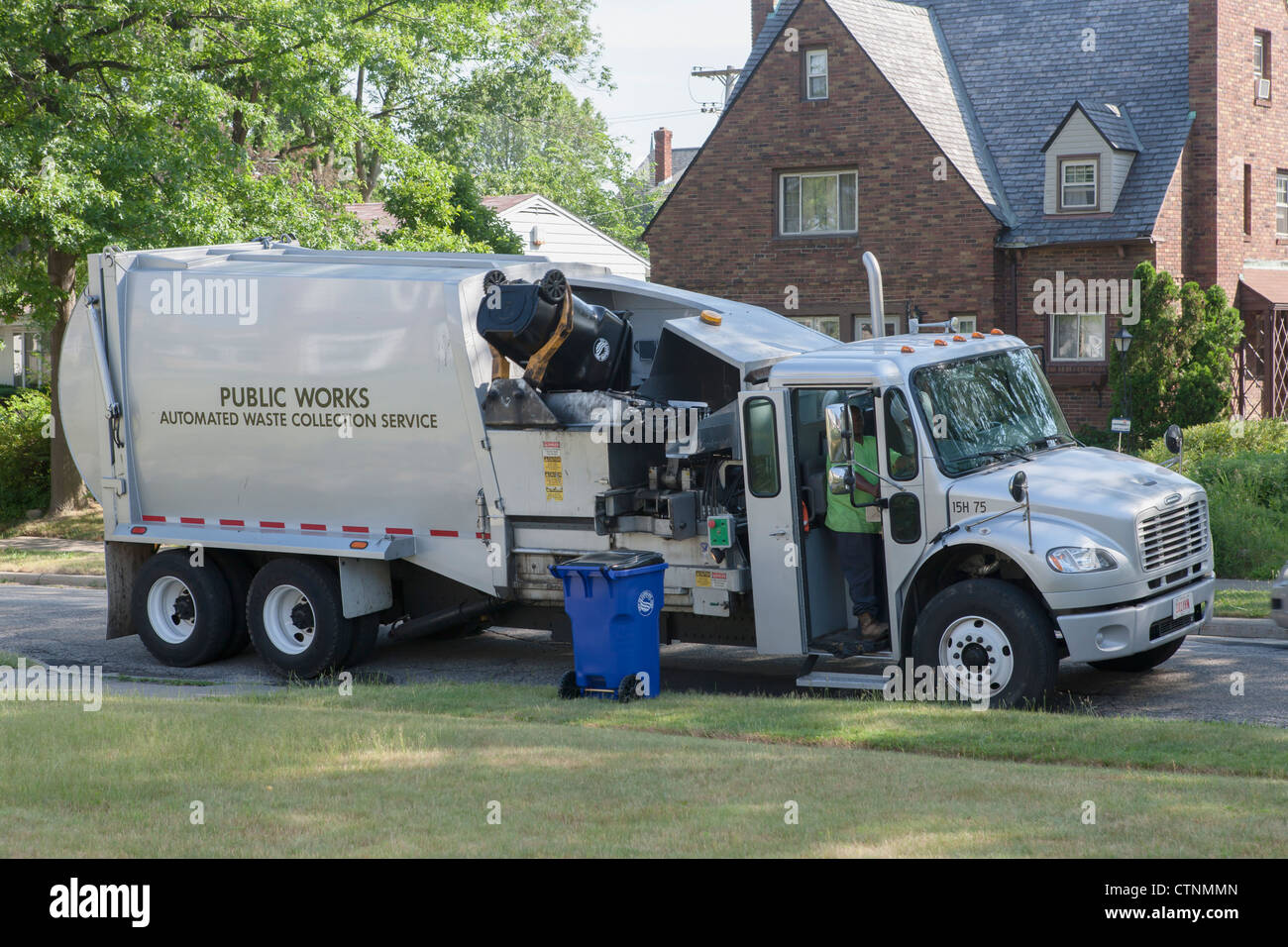 Waste collection workers pick up a black waste cart on a suburban street using an automated truck in Cleveland, Ohio. Stock Photo