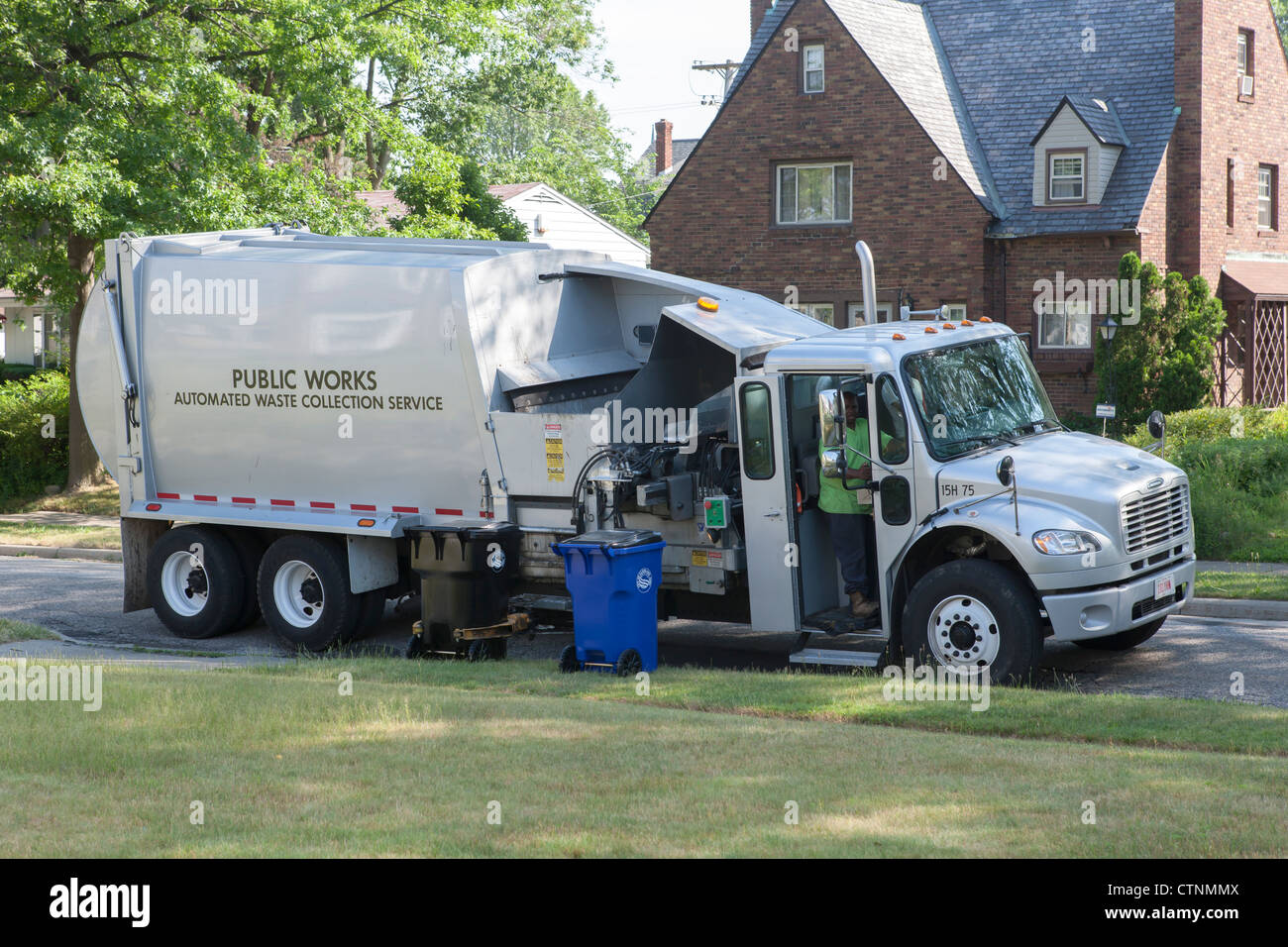 Waste collection workers pick up a black waste cart on a suburban street using an automated truck in Cleveland, Ohio. Stock Photo