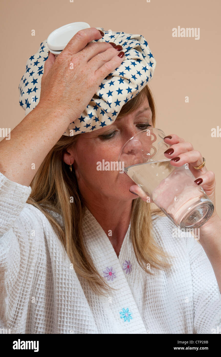 Woman with ice pack on head suffering a hangover and drinking a glass