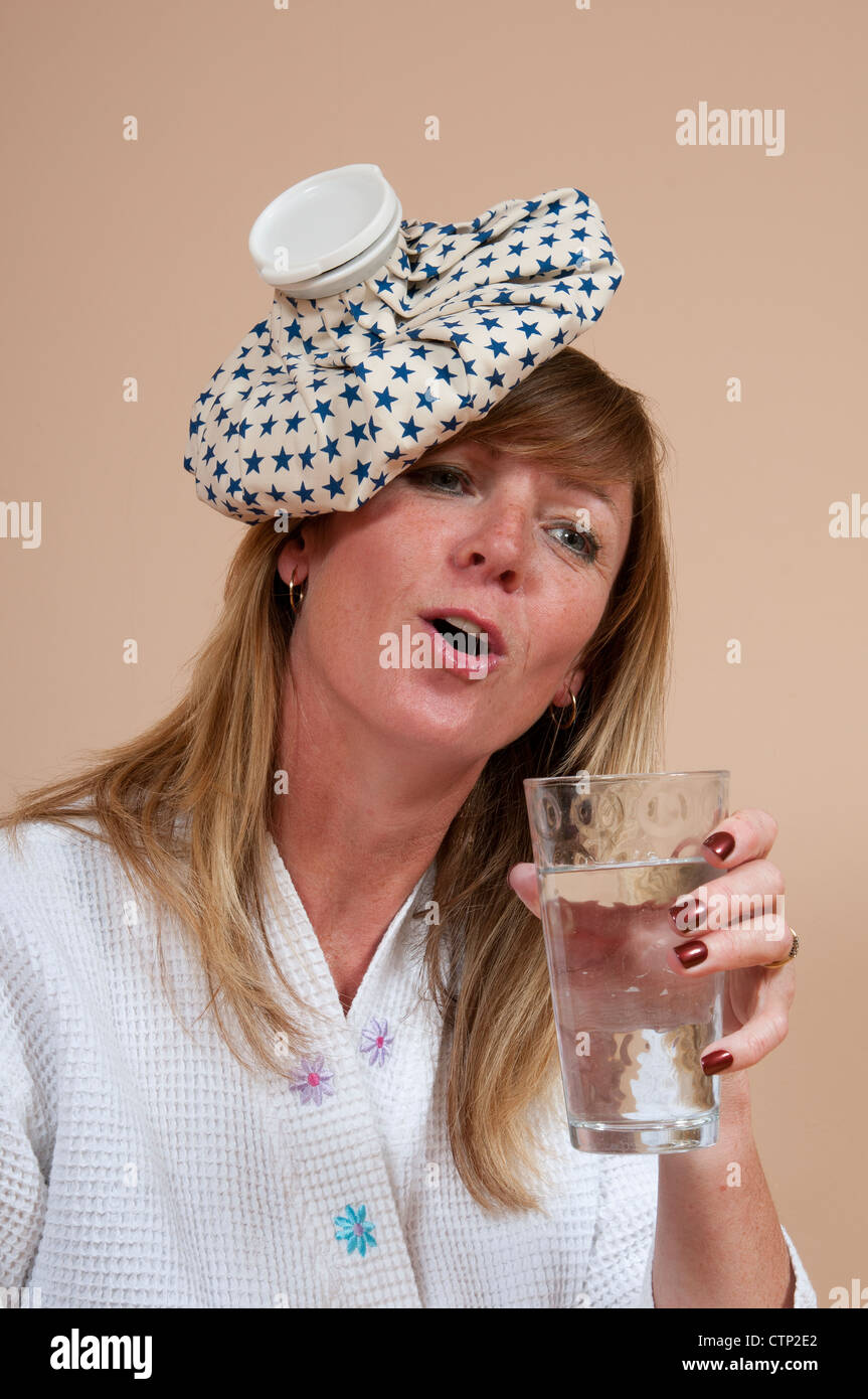 Woman with ice pack on head suffering a hangover and drinking a glass