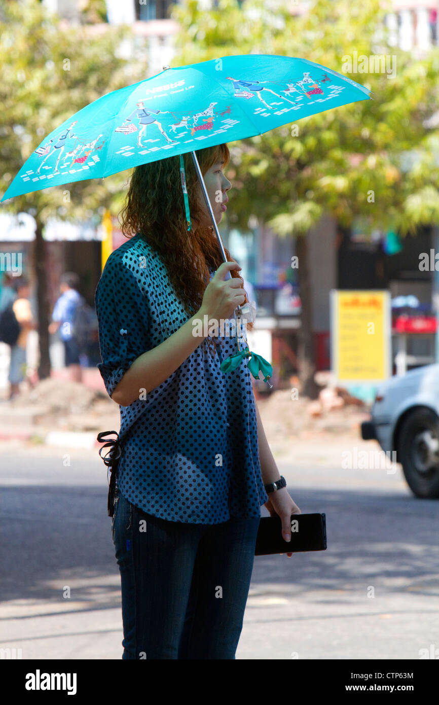 Burmese woman walking under the shade of an umbrella in (Rangoon) Yangon, (Burma) Myanmar. Stock Photo
