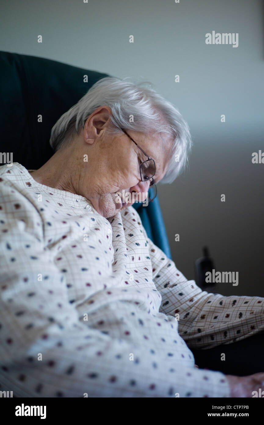 Old woman slumped over asleep in chair Stock Photo