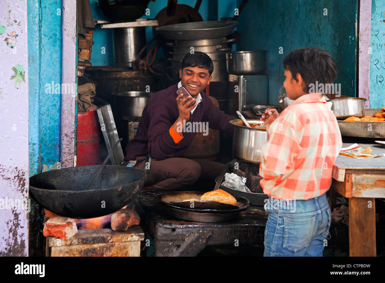 Boy preparing food while making a call with his cellular phone in Old Delhi, India Stock Photo