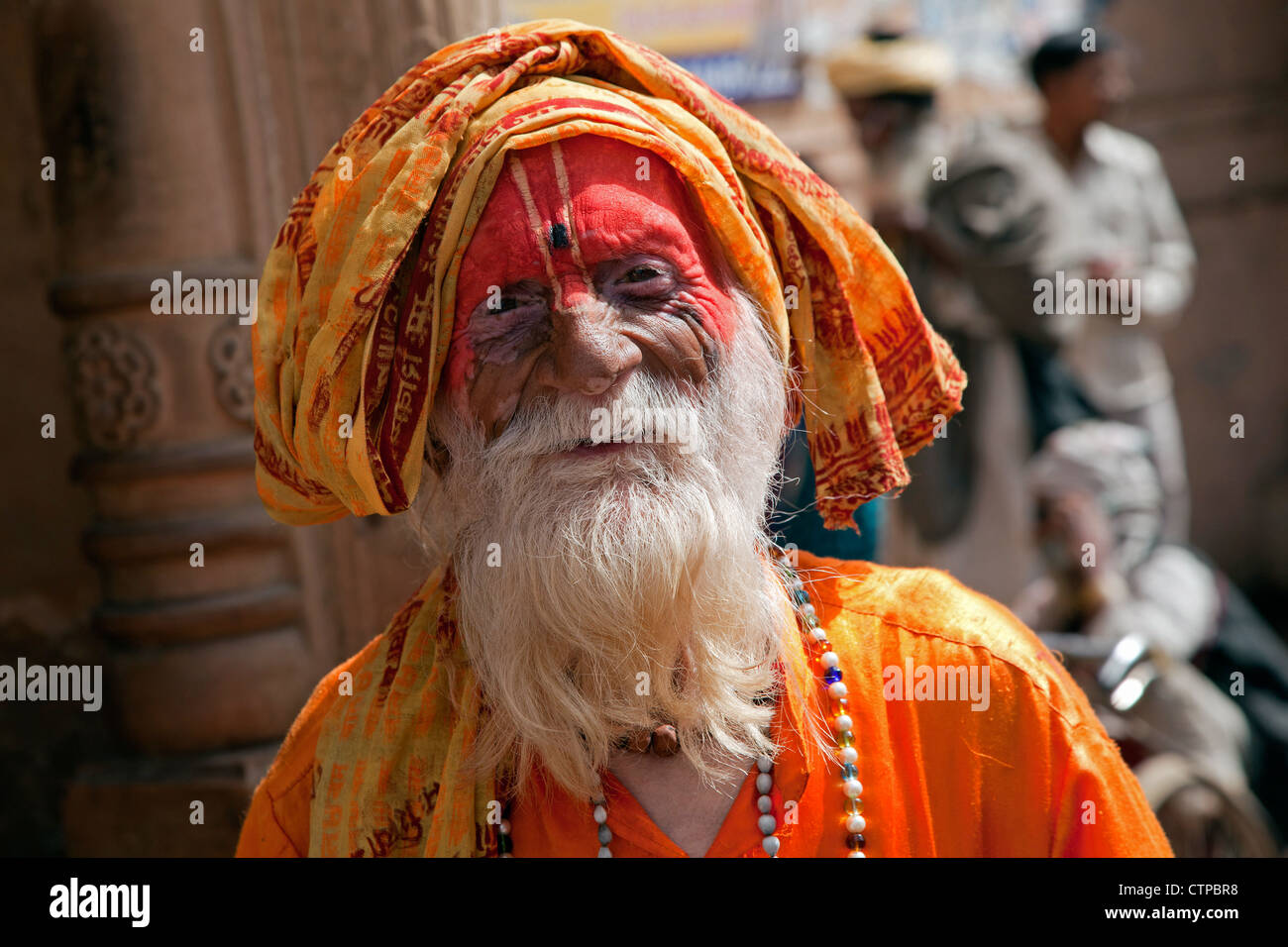 Portrait of old Hare Krishna follower with grey beard dressed in orange dress in front of temple in Govardhan, India Stock Photo