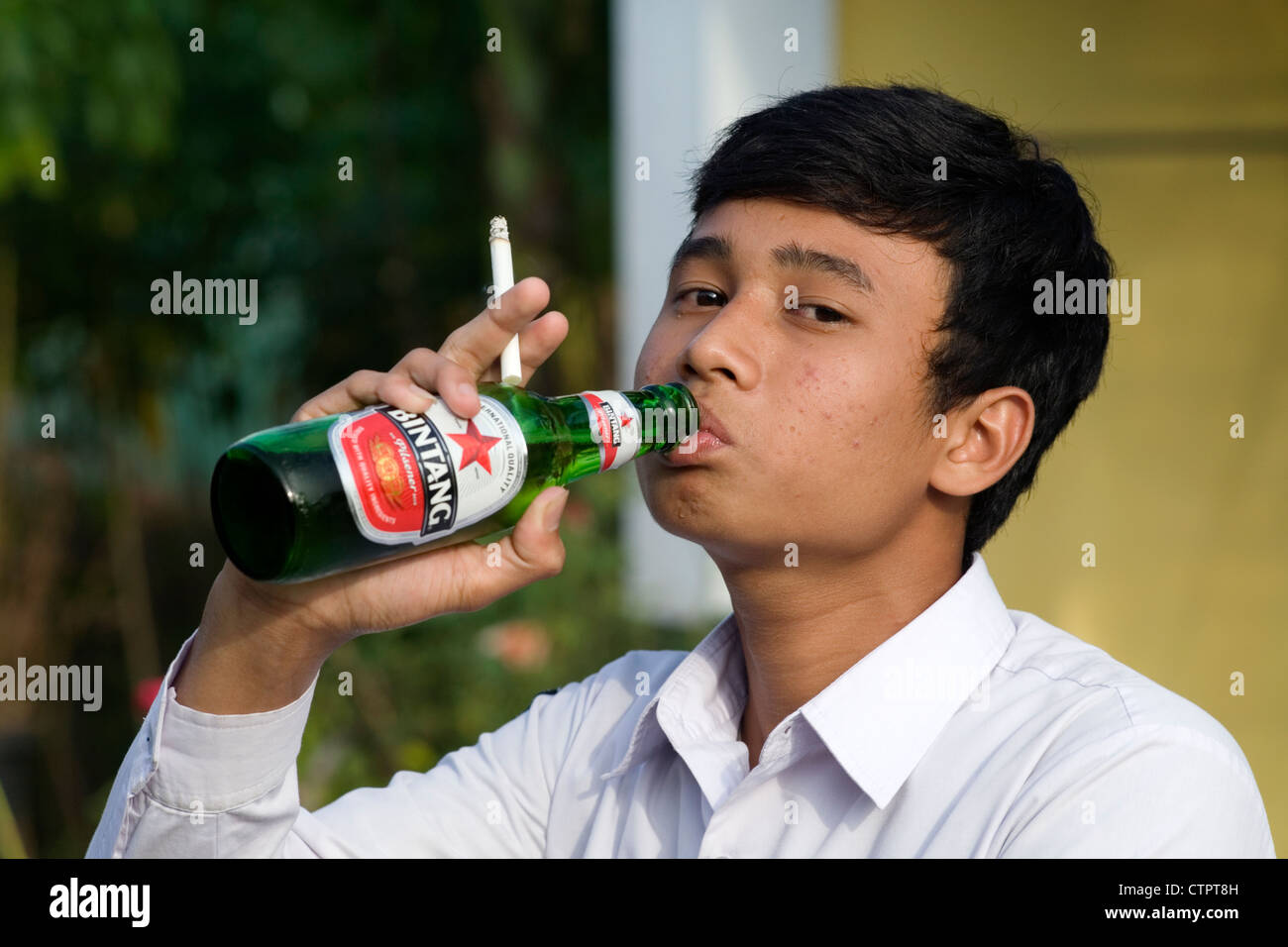 young indonesian schoolboy in uniform smoking and drinking beer Stock