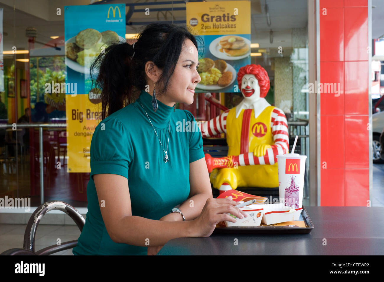 local woman relaxes with a cigarette after eating a meal at her table in  macdonalds java indonesia Stock Photo