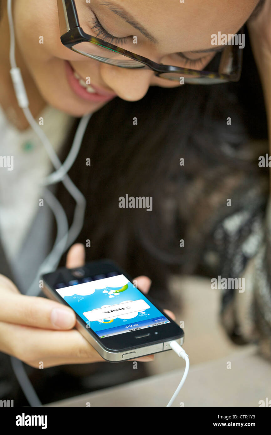 Smiling young female wearing headphone making phone call using Skype with iphone 4 Stock Photo