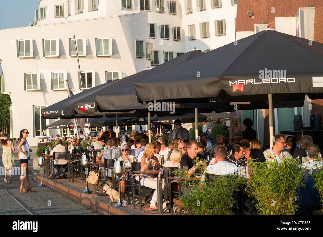 Busy restaurants at Neuer Zollhof buildings designed by Frank Gehry in Medianhafen in Dusseldorf Germany Stock Photo