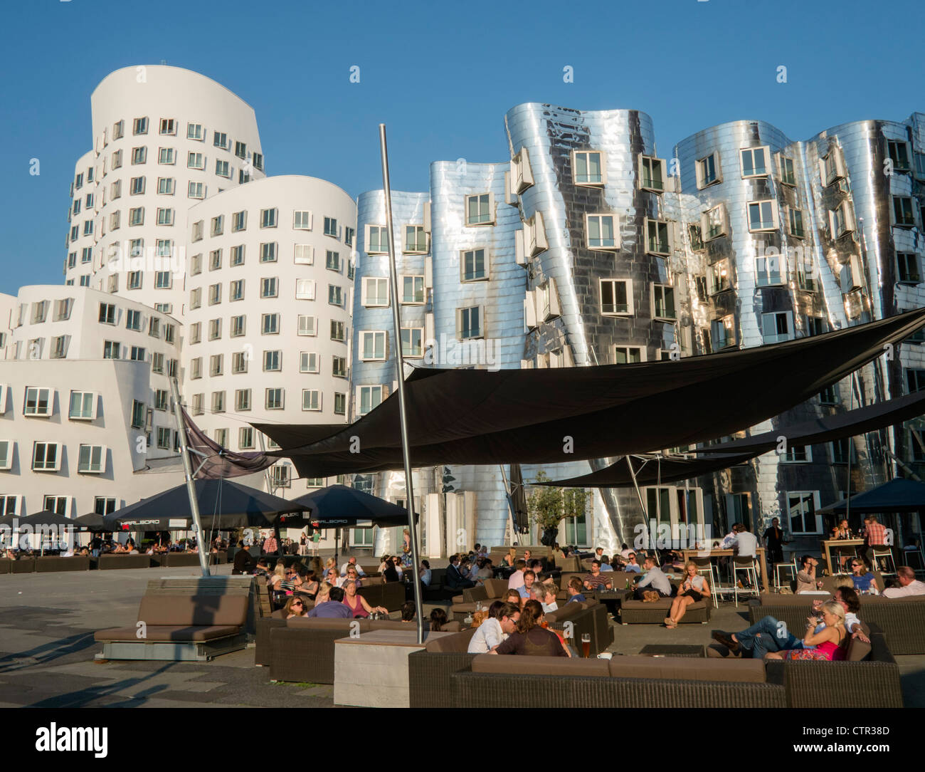 Busy bars in evening at Neuer Zollhof buildings designed by Frank Gehry in Medianhafen in Dusseldorf Germany Stock Photo