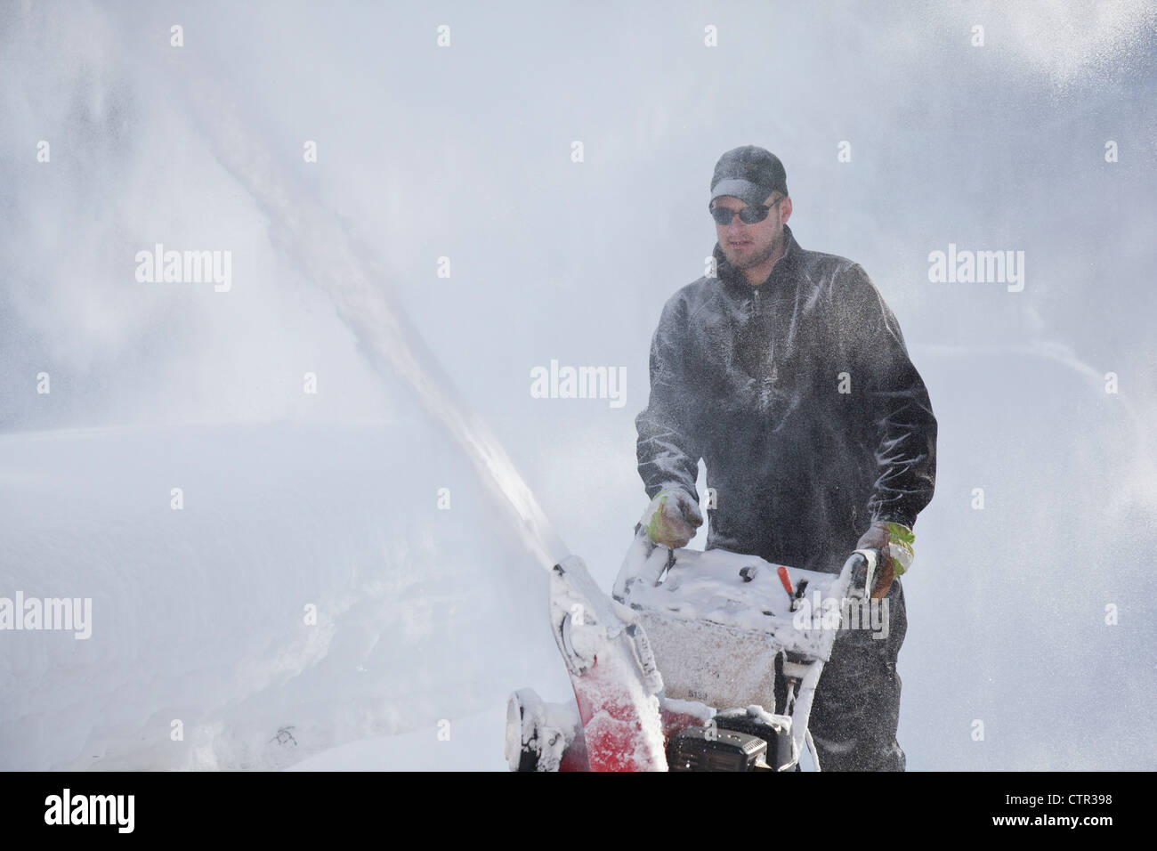Man uses a snowblower to clear a driveway after a big snowfall