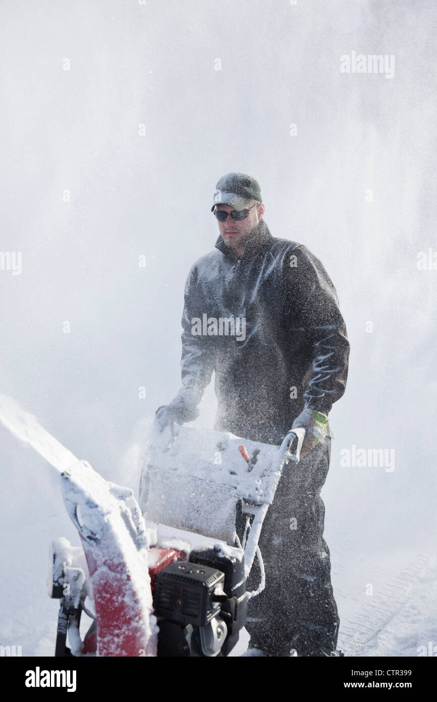 Man uses a snowblower to clear a driveway after a big snowfall