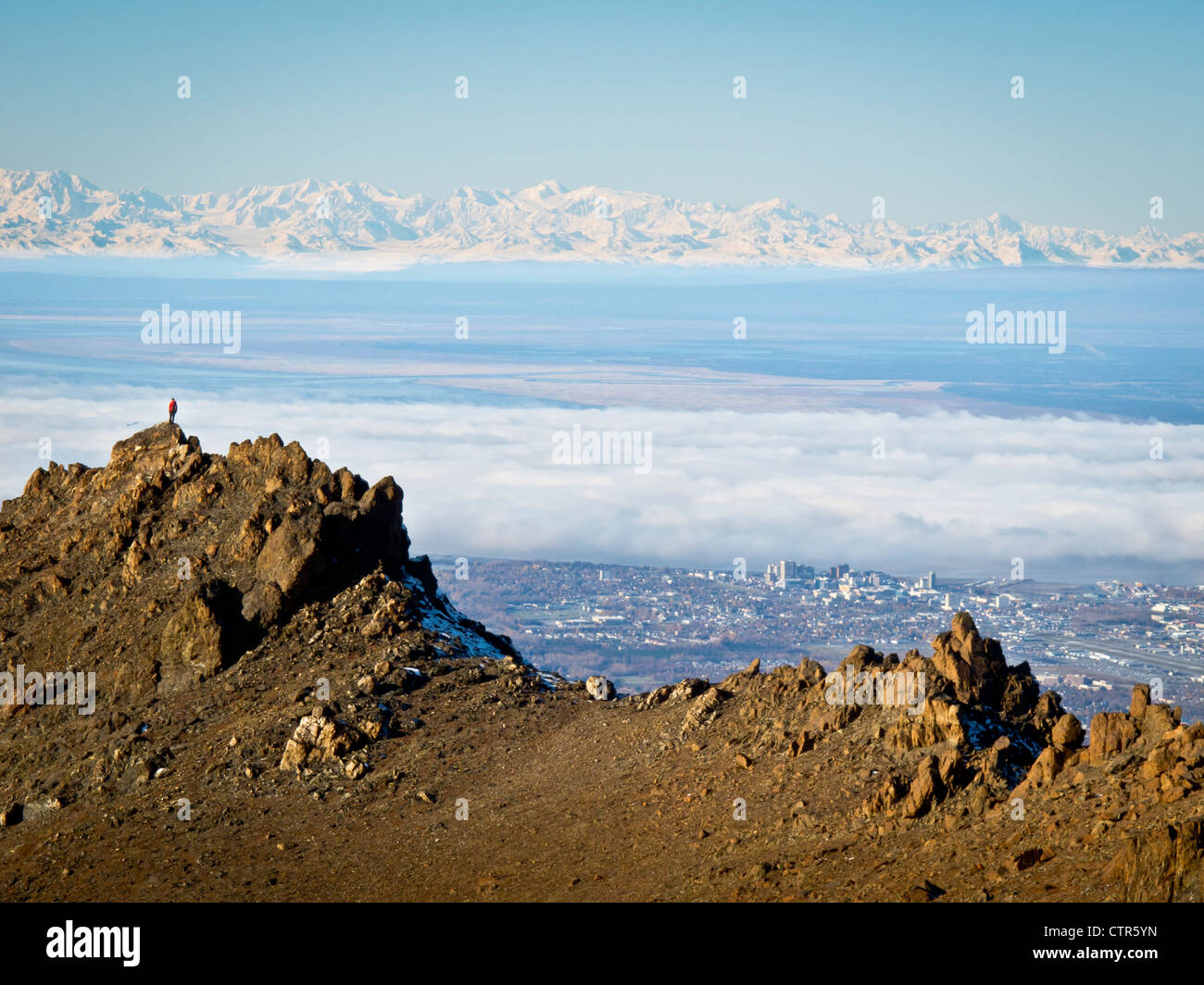 Woman trail runner stands on rock ridge high above Anchorage Alaska Range beyond Chugach Mountains Southcentral Alaska Autumn Stock Photo