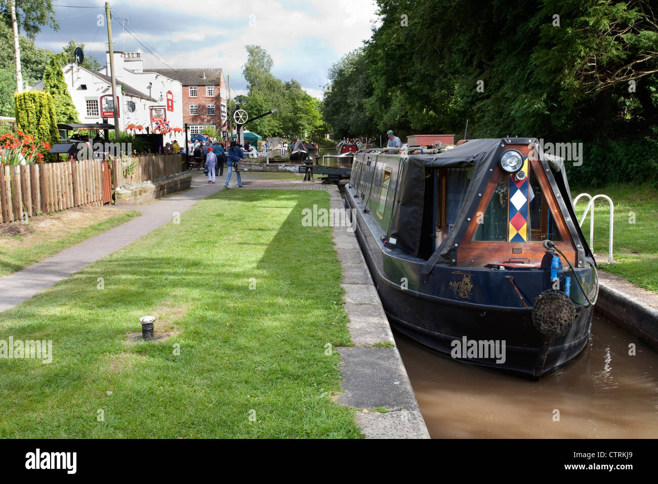A canal boat approaching locks on the Shropshire Union canal near the Shroppie Fly public house, Audlem, Cheshire. Stock Photo