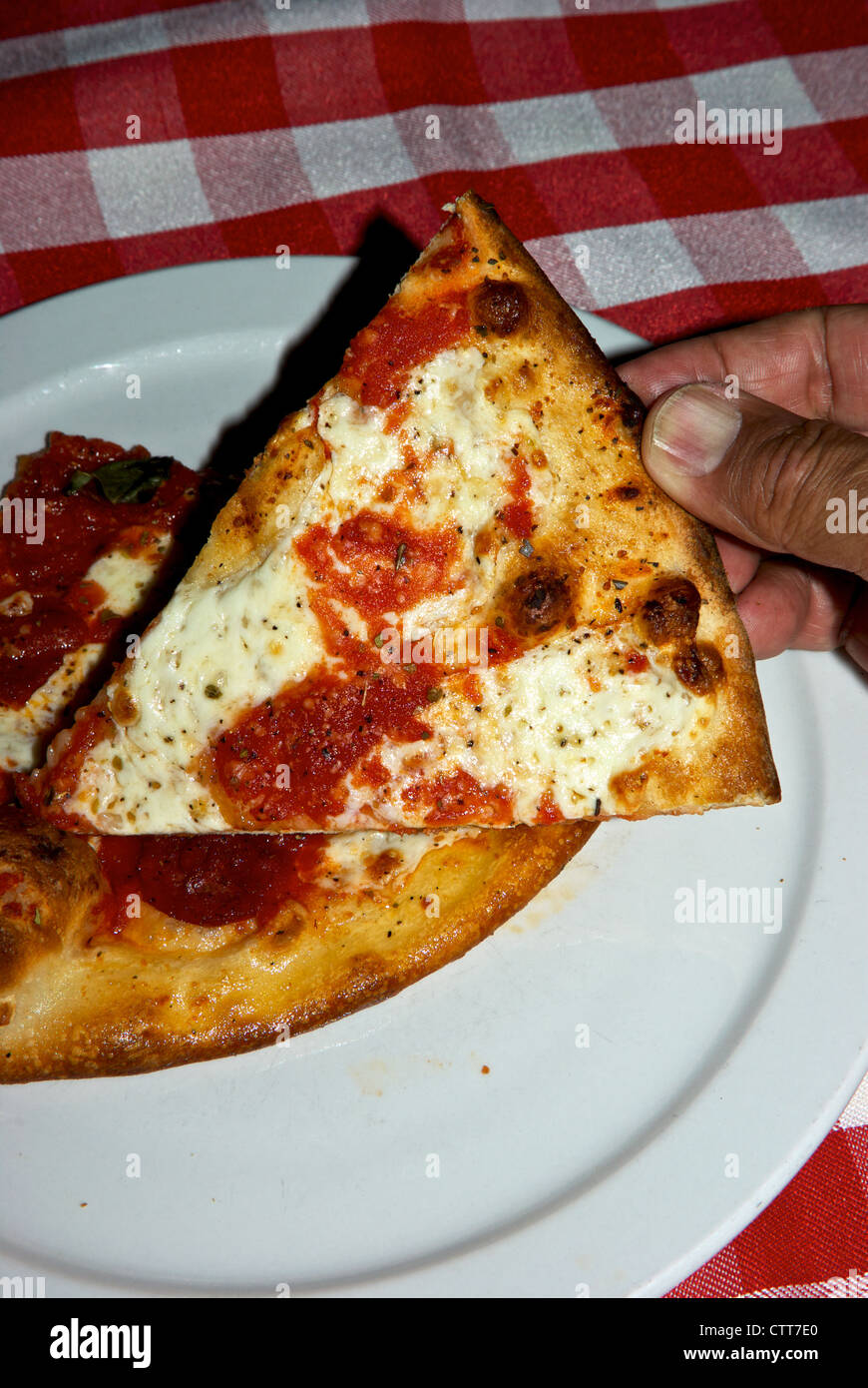 Hand holding slice plain mozarella cheese pizza over plate at Grimaldi's restaurant Old Town Scottsdale AZ Stock Photo