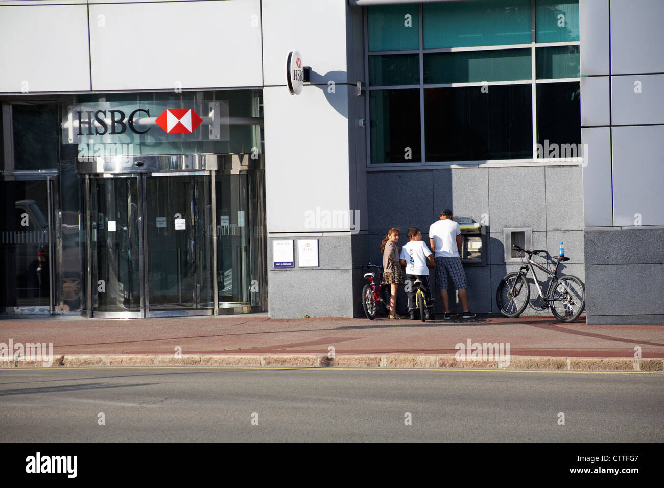 Family with pushbikes using cash machine ATM at HSBC bank in St Helier, Jersey, Channel Islands, UK in July Stock Photo