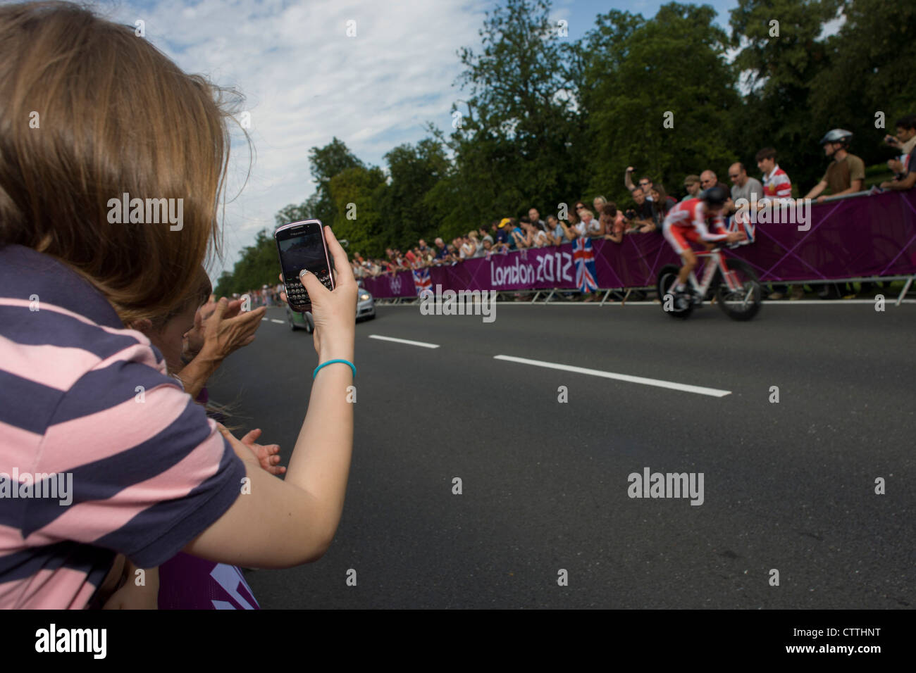 A young girl uses her Blackberry Curve to films cyclists as they race past fans lining the route through Bushy Park in south west London, during the London 2012 Olympic 44km men's cycling time trial, eventually won by Team GB's Bradley Wiggins. Stock Photo