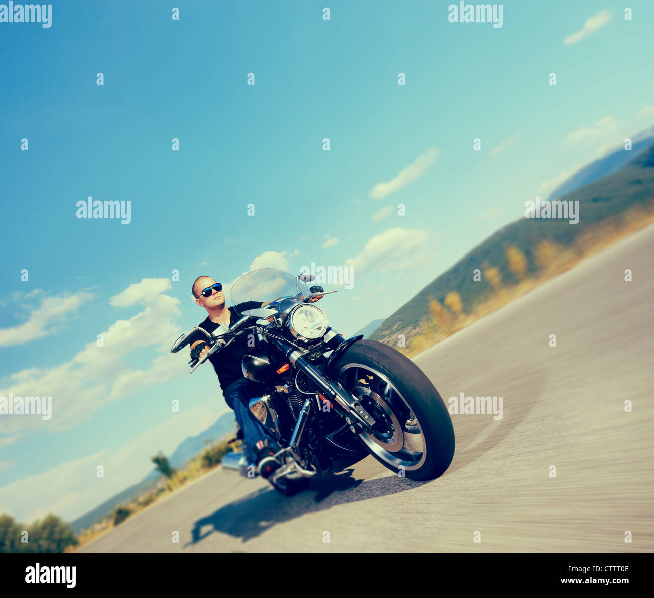 Biker riding a customized motorcycle on an open road shot with a tilt and shift lens and with very shallow depth of field Stock Photo