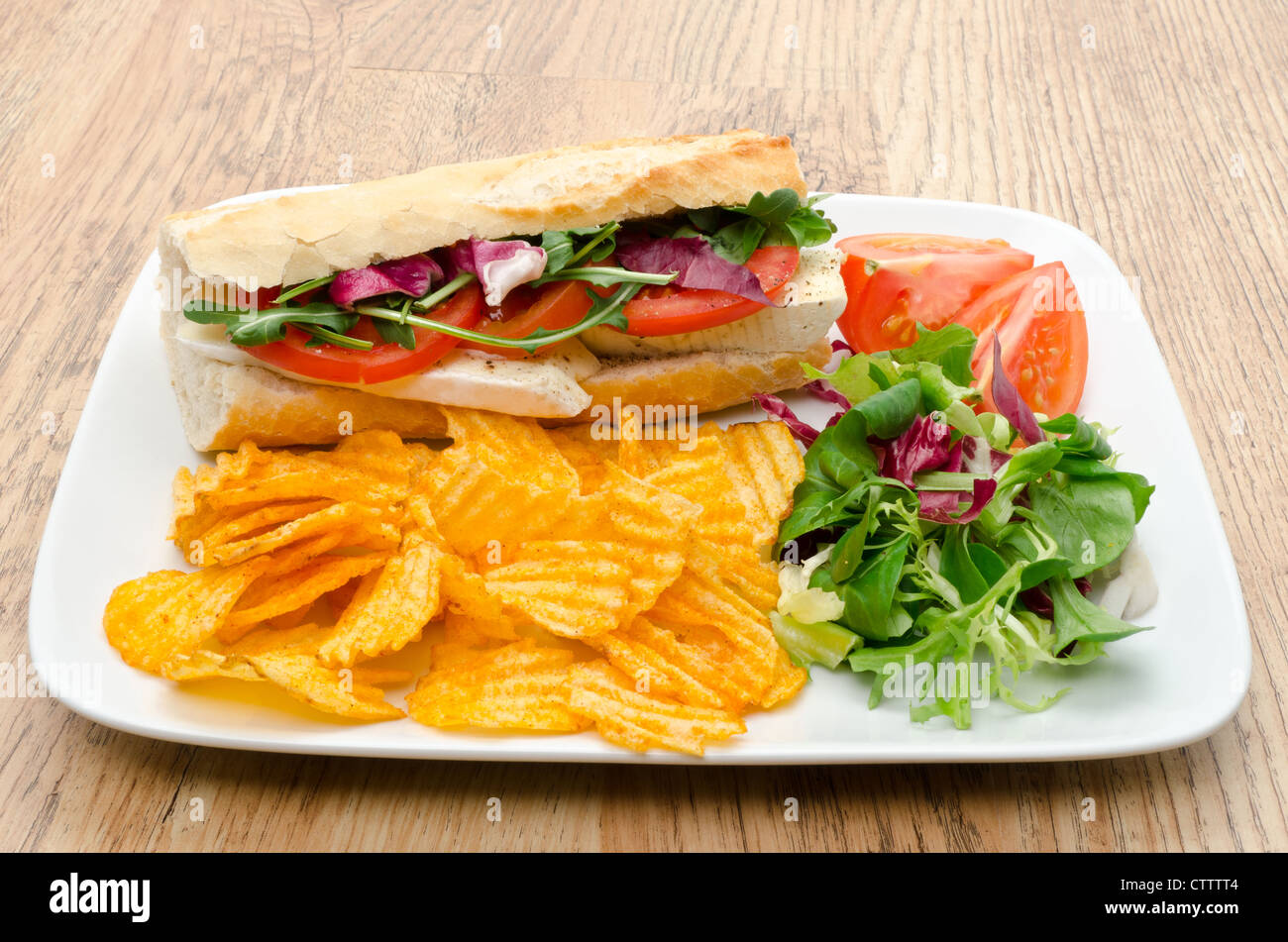 Baguette filled with Brie cheese served with salad and flavoured chips studio shot Stock Photo
