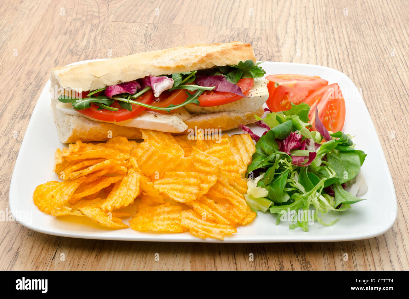 Baguette filled with Brie cheese served with salad and flavoured chips - studio shot Stock Photo
