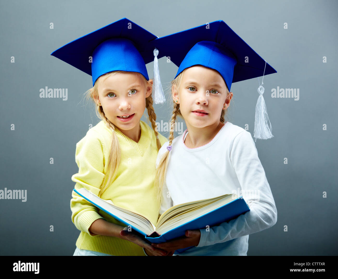 Portrait of lovely twin girls in hats with tassels holding open book Stock Photo