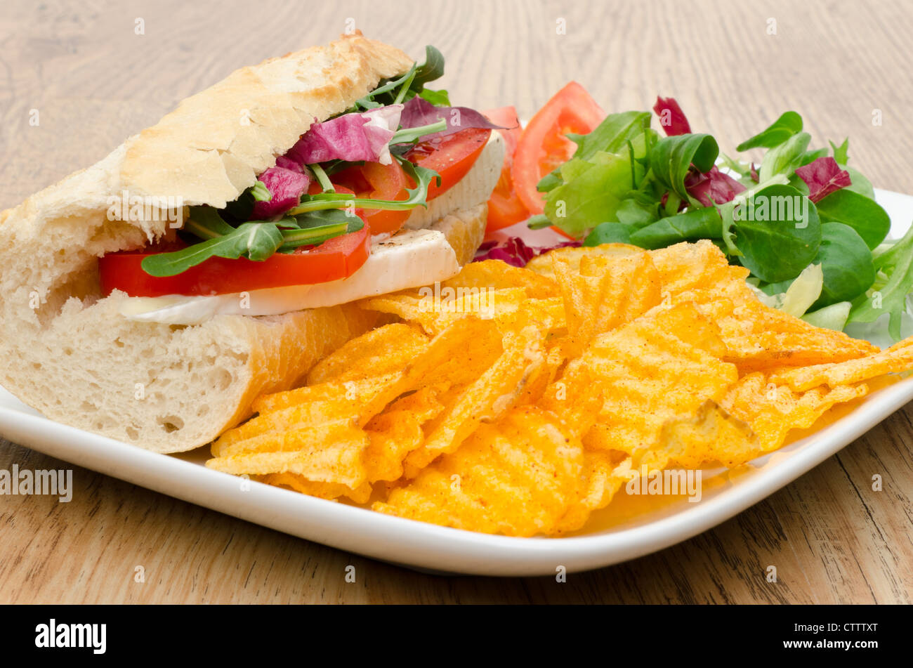 Baguette filled with Brie cheese served with salad and flavoured chips - studio shot Stock Photo