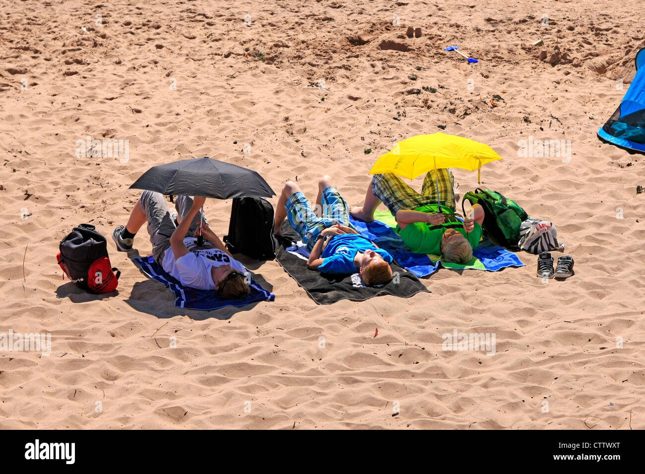 Three teenage boys using Umbrellas as shades from the sun on Exmouth