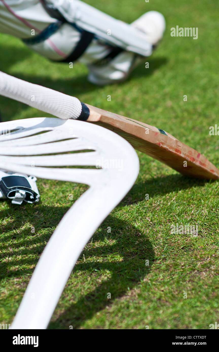 Cricket bat leans on the back of a fallen plastic chair. A cricketer's