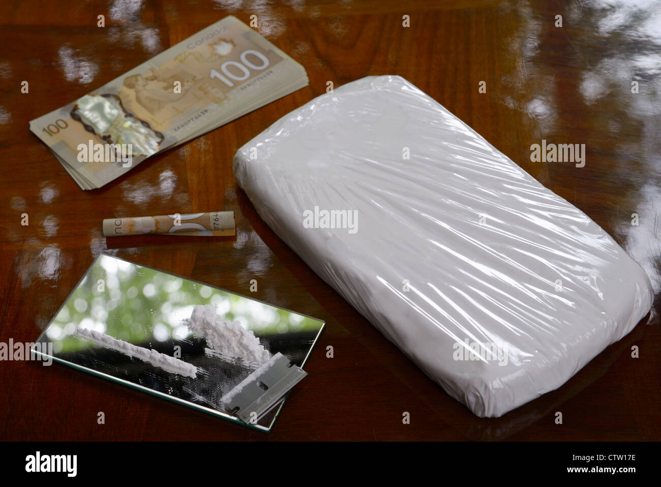 Large bag of cocaine drug with hundred dollar Canadian bills cash money and coke line with razor blade on table Stock Photo