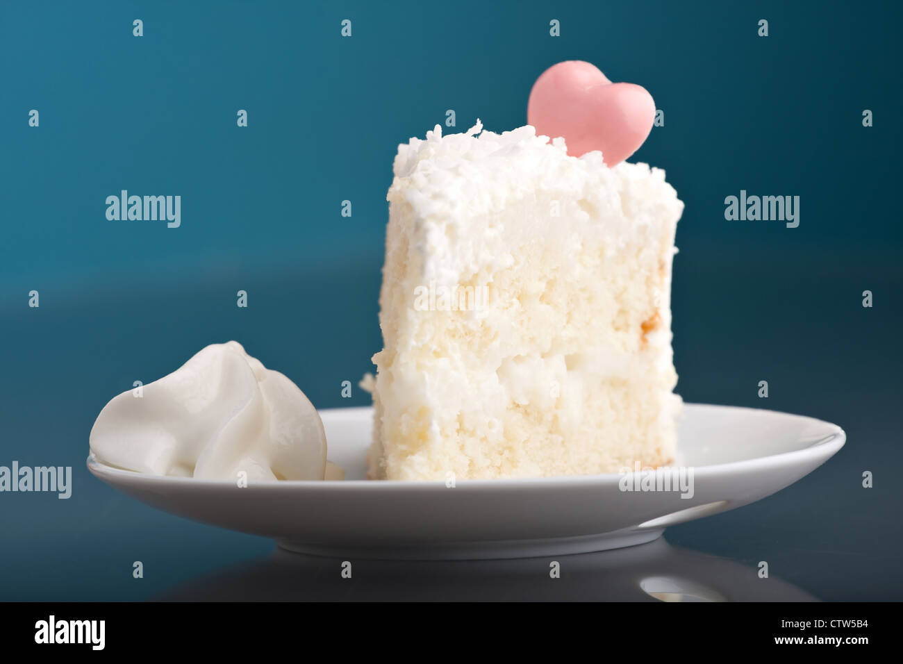 A fresh piece of coconut cream cake on a white plate with a bit of whipped cream on the side. Stock Photo