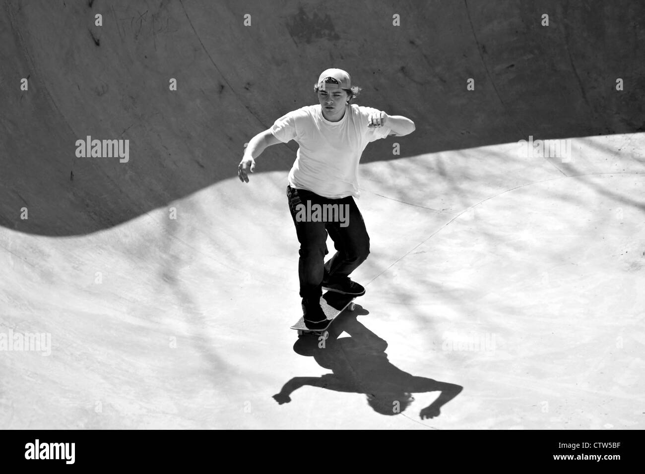 Black and white of a young skateboarder skating in the bottom of the bowl at a concrete skate park. Stock Photo