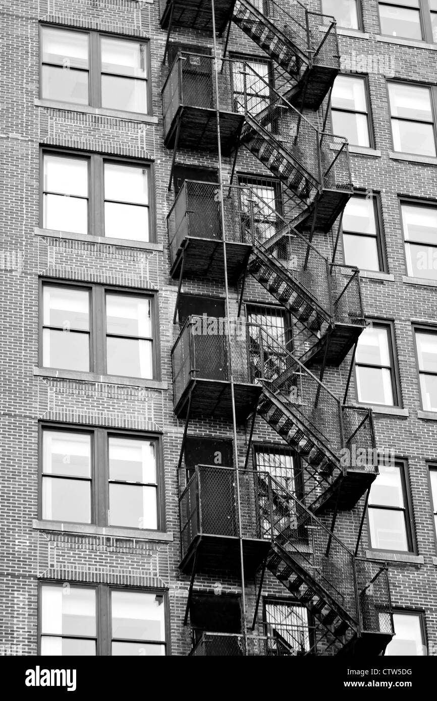 Exterior fire escape stairs on the outside of an old brick building in black and white. Stock Photo