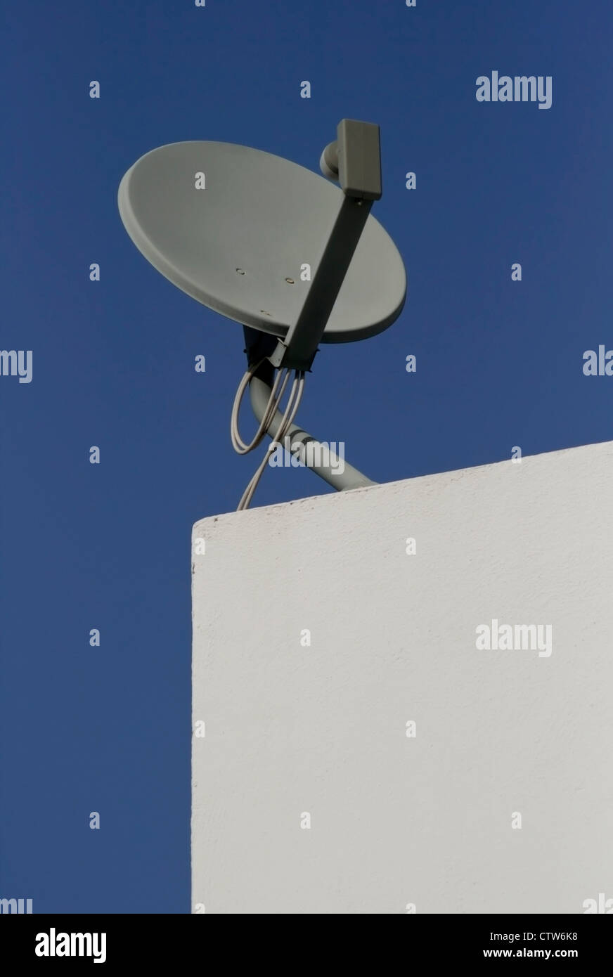 Grey satellite dish on blank white exterior wall against blue sky with copy space. Stock Photo