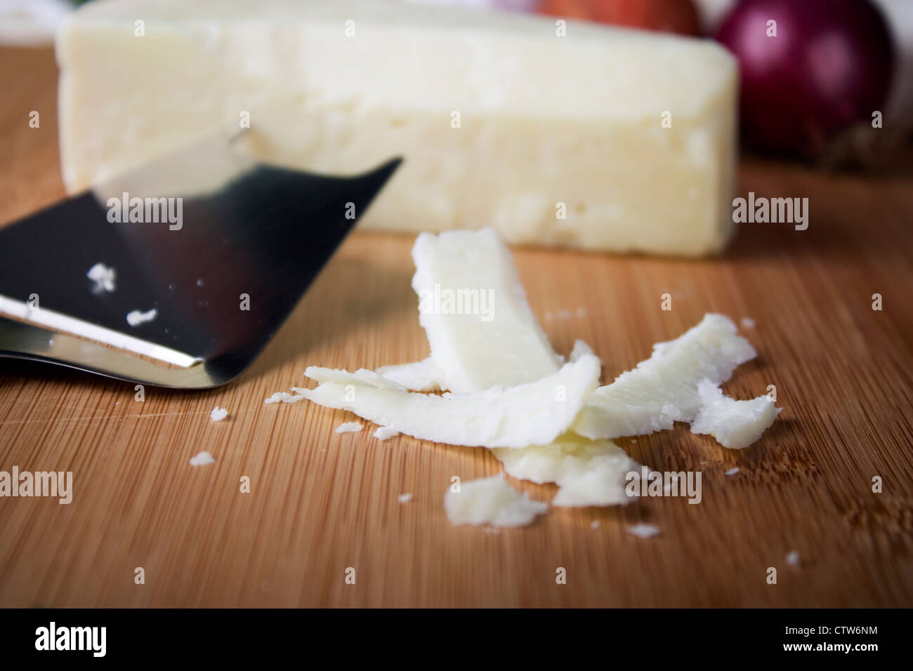 Flakes of Italian cheese on cutting board with cheese slicer and block of cheese in background. Shallow depth of field. Stock Photo