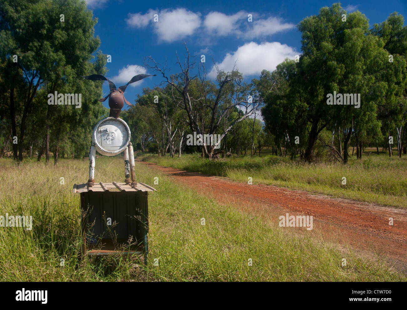 Cow sculpture roadside mailbox made partly out of metal barrel with typical red dirt track leading to property Queensland Austra Stock Photo