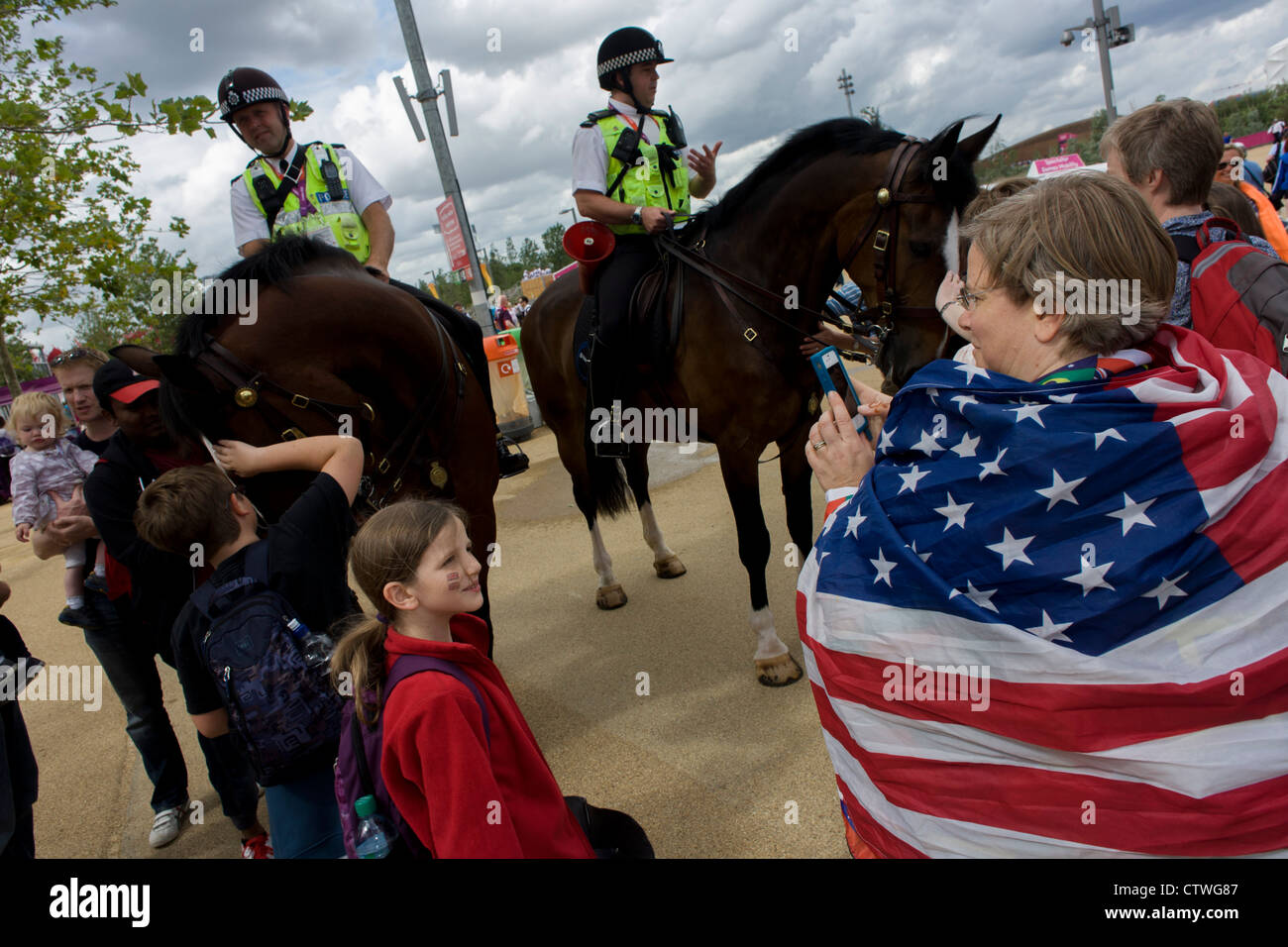 American spectators admire mounted police officers on horseback help control crowds and provide security in the Olympic Park during the London 2012 Olympics. This land was transformed to become a 2.5 Sq Km sporting complex, once industrial businesses and now the venue of eight venues including the main arena, Aquatics Centre and Velodrome plus the athletes' Olympic Village. After the Olympics, the park is to be known as Queen Elizabeth Olympic Park. Stock Photo