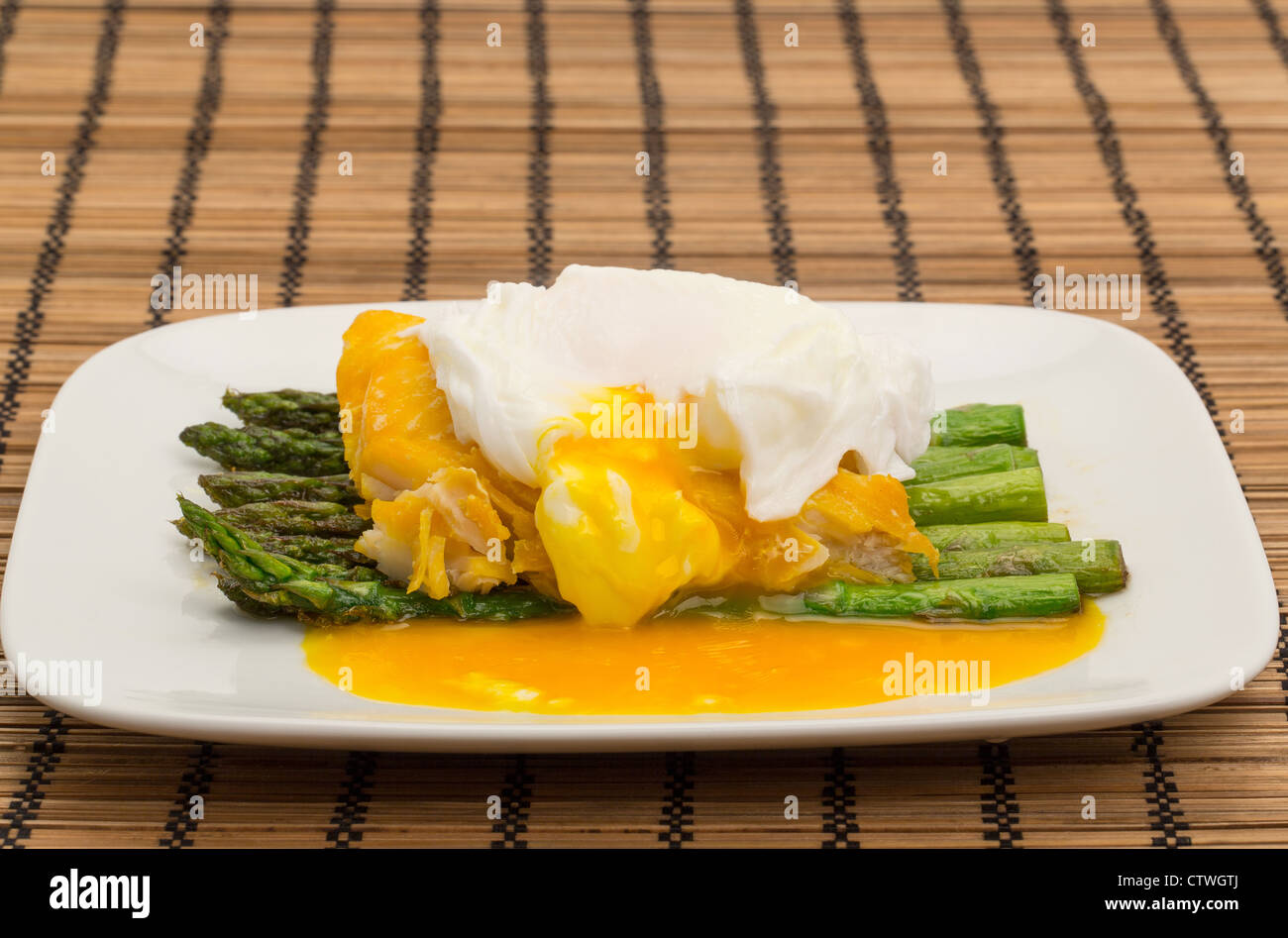 Smoked haddock, asparagus and a poached egg dinner arranged on a china plate with the yolk draining from the poached egg Stock Photo