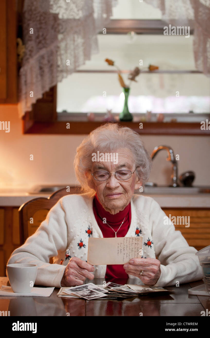 Elderly woman sitting in her kitchen and holding an old picture and ...