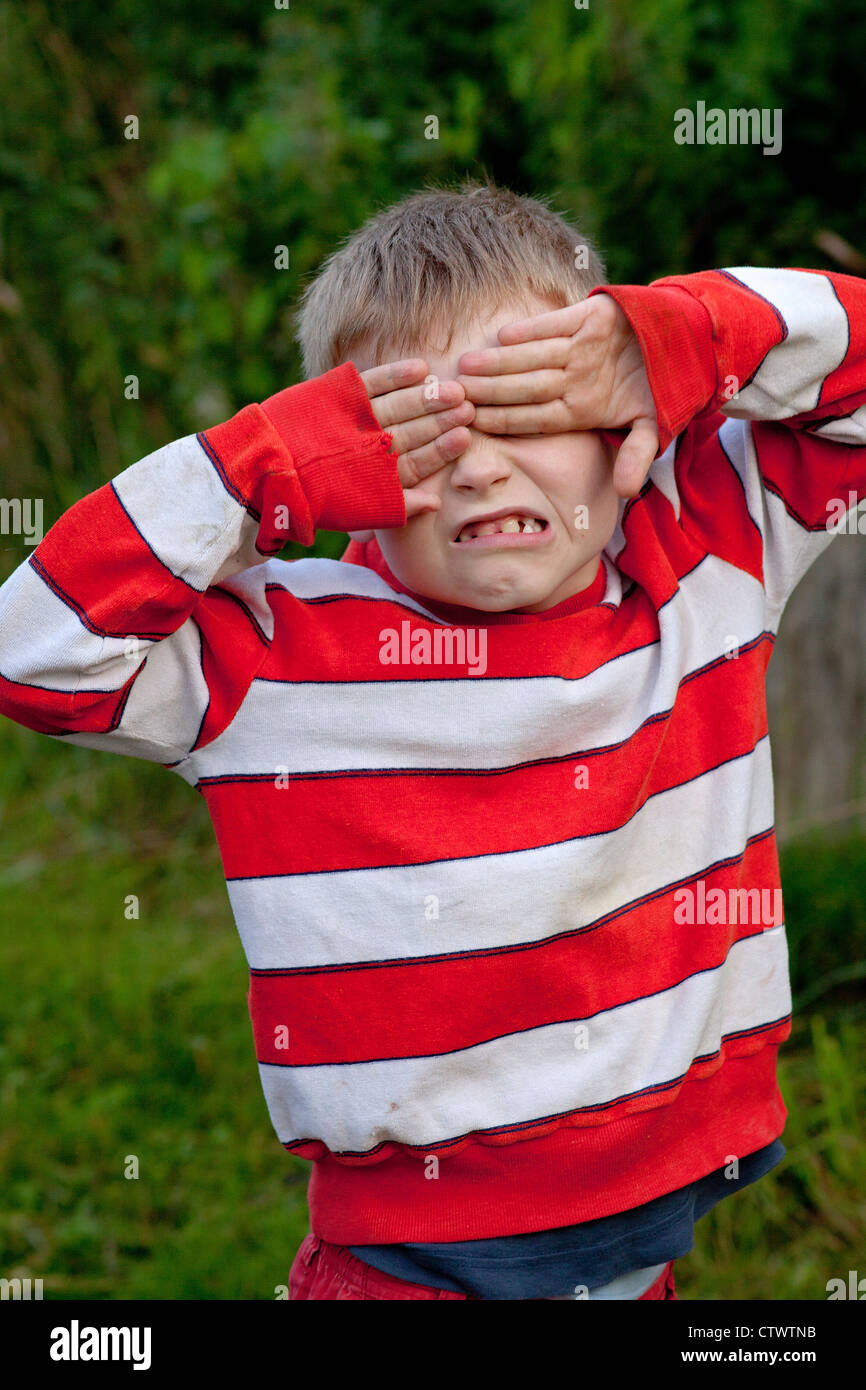 young boy covering his eyes with his hands making a face Stock Photo