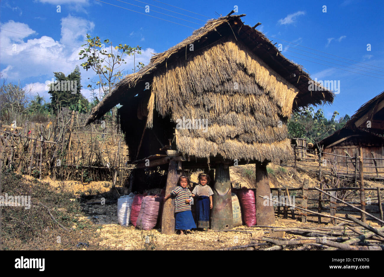 Laotian Sisters Pose next to a Thatched Rice Store or Agricultural Building Raised on Recycled Cluster Bombs or Metal War Waste near Phonsavan Laos Stock Photo
