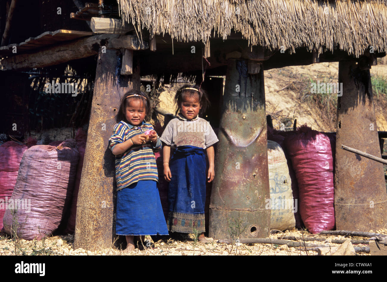Young Twins or Lao Girls Pose Between Cluster Bomb Casings Used to Support a Thatched Rice Store near Phonsavan Laos Stock Photo