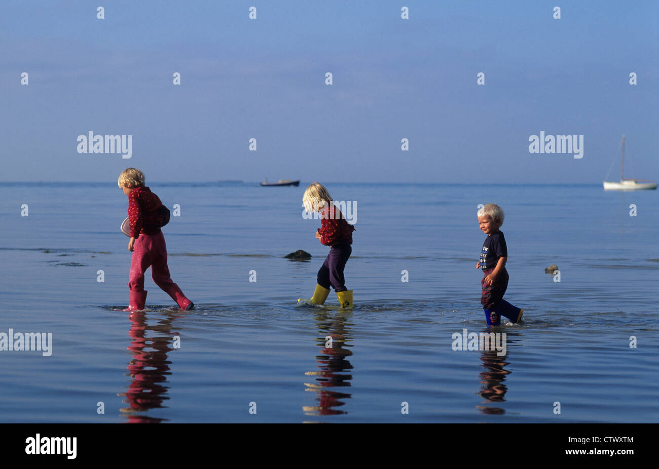 Three siblings playing follow my leader in the shallows of the sea