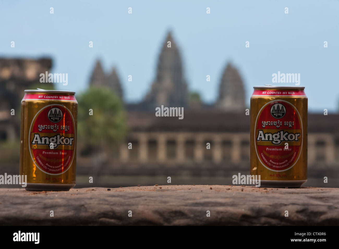 Cans of Angkor beer with tower symbol frame the actual towers of the Angkor Wat temple. Stock Photo
